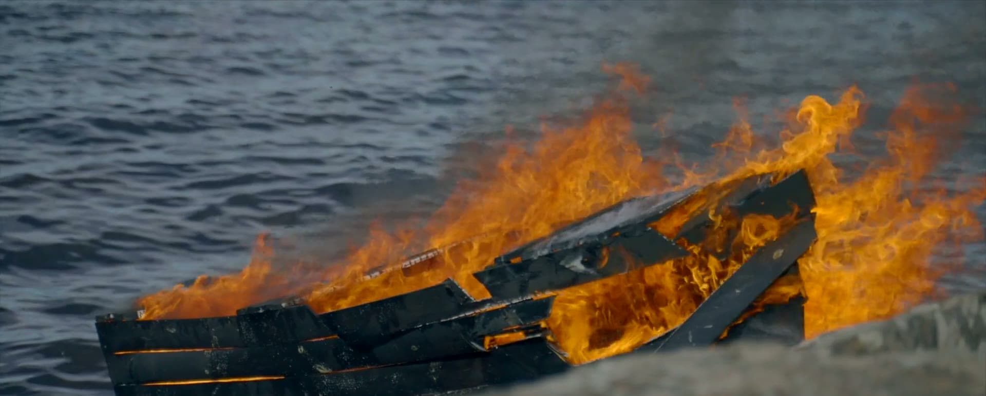 Music video still: a burning boat at sea